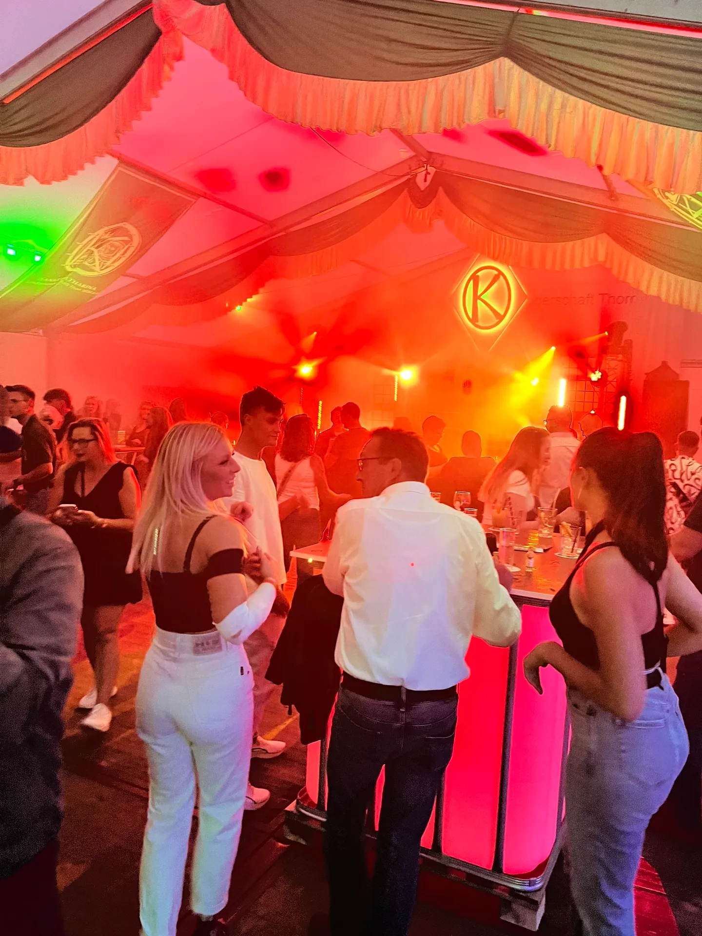Volle Tanzfläche der Sommernacht-Feier in rotem Bühnenlicht, Tänzer vor dem K-Wappen
