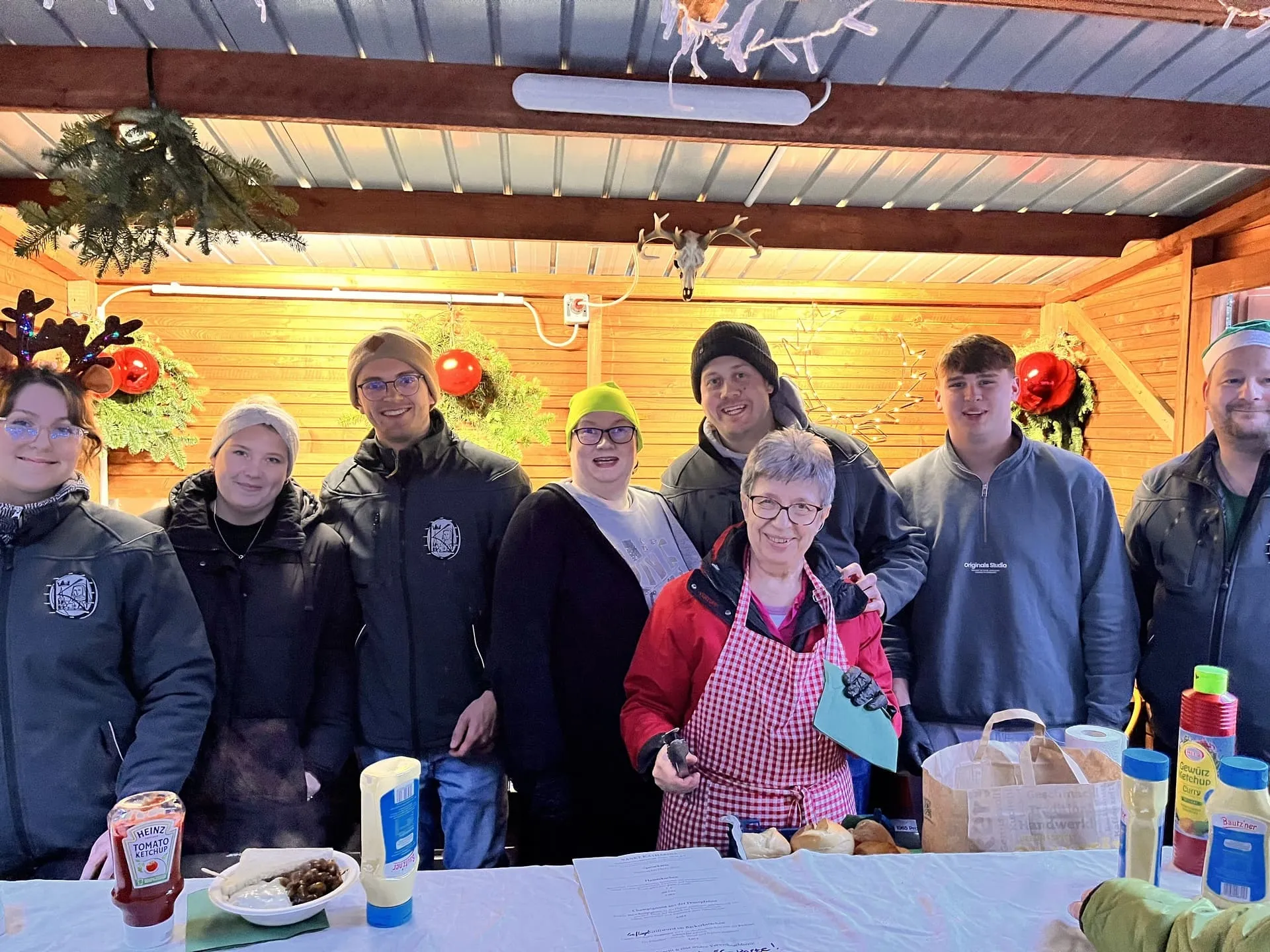 Helfer am Stand der Bruderschaft auf dem Weihnachtsmarkt, dahinter weihnachtliche Dekoration