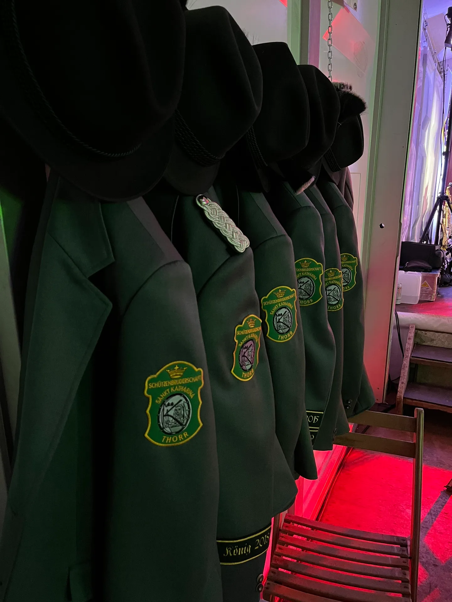 Uniformjacken mit Vereinswappen und Schützenhüte hängen aufgereiht in der Garderobe