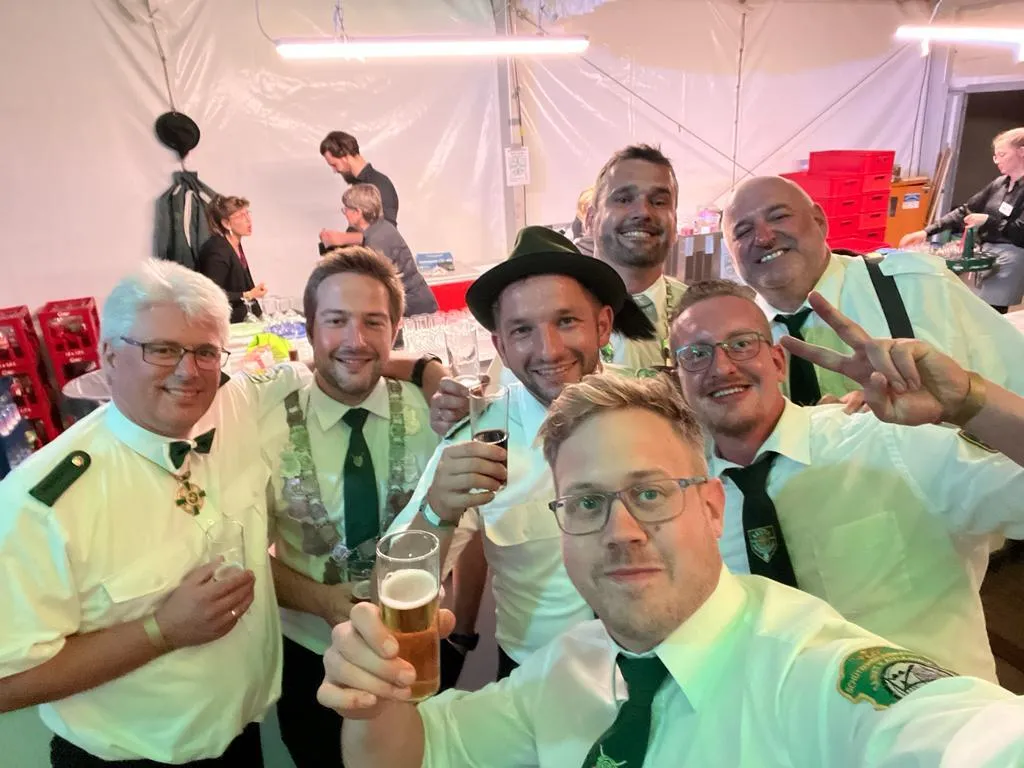 Selfie von sieben Schützenbrüdern in weißen Hemden und Krawatte mit Bier- und Schnapsgläsern hinter der Theke einer befreundeten Bruderschaft