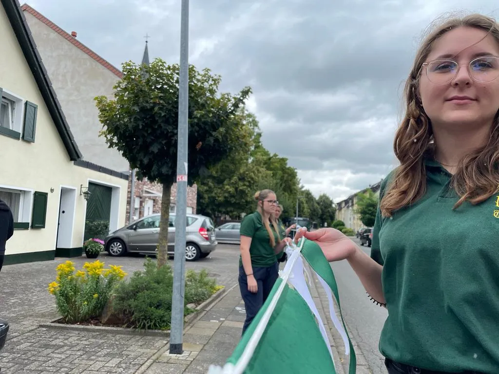 Junge Schützenschwester hält eine grün-weiße Wimpelkette zum Anbringen an einem Laternenmast in der Dorfstraße