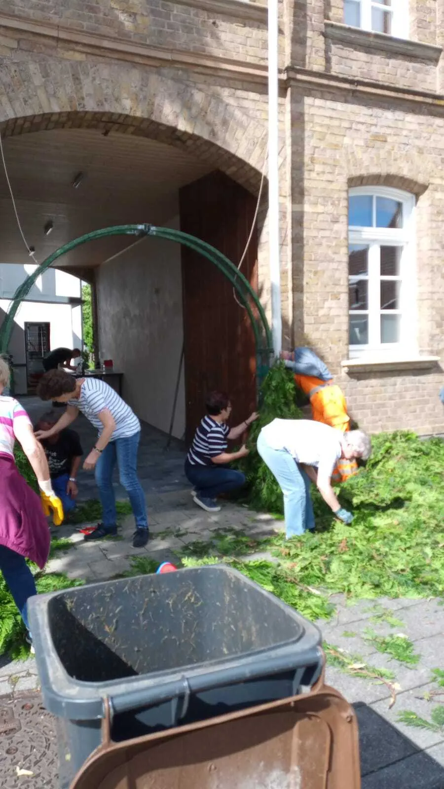 Mehrere Helfer arbeiten gemeinsam am Drahtgeflecht-Bogen für den Königsschmuck