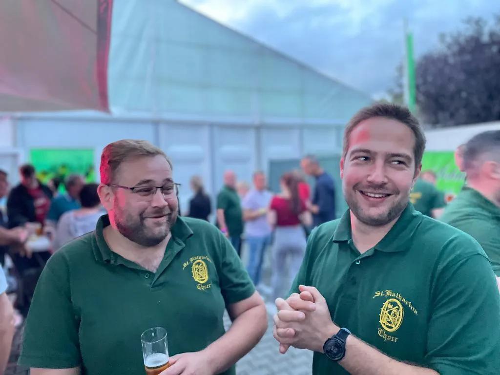 Zwei Schützenbrüder im Vereins-Polo unterhalten sich vor dem Festzelt, im Hintergrund weitere Gäste