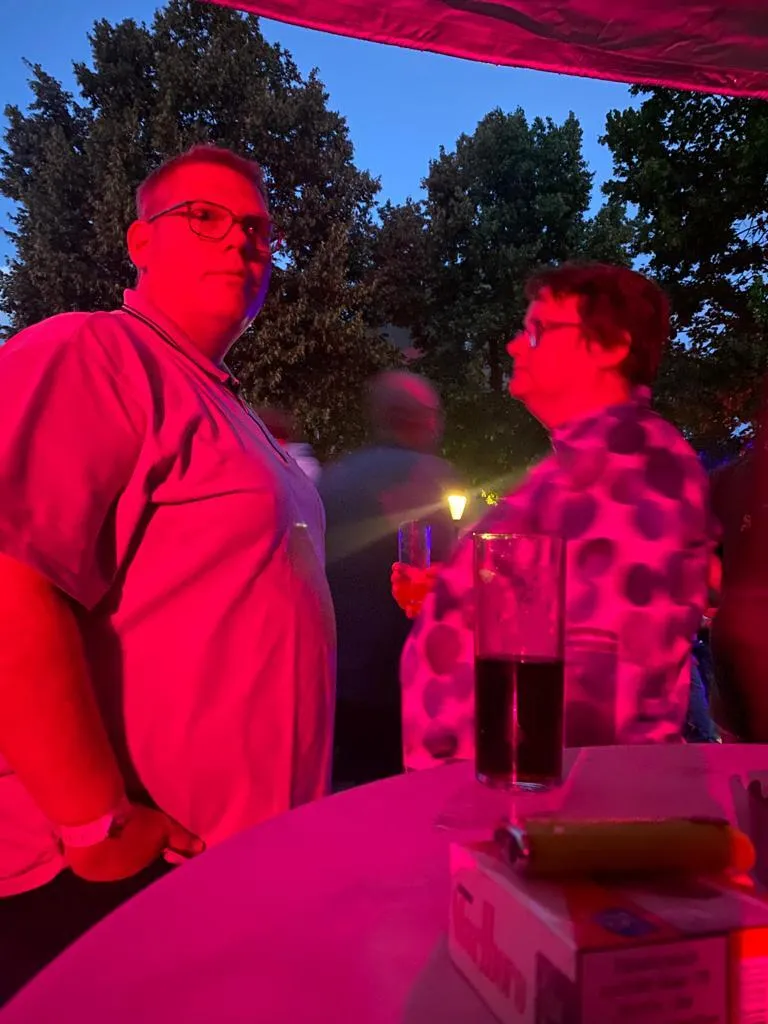 Zwei Vereinsmitglieder mit Longdrink-Gläsern im rot-pinken Licht der Sommernacht 2023