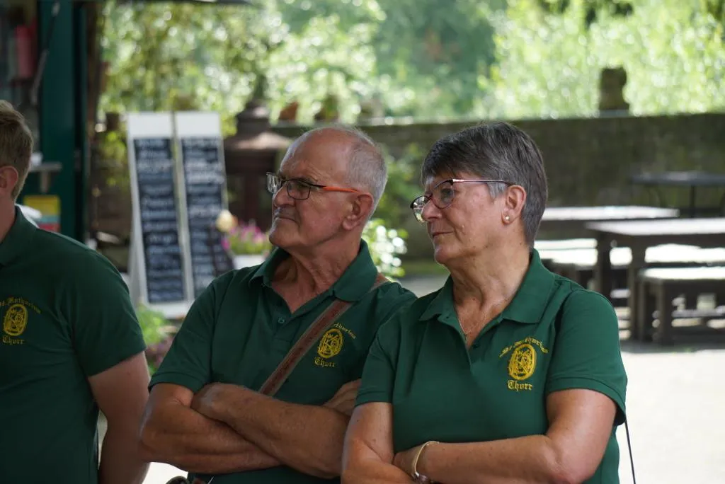 Zwei Vereinsmitglieder im Vereins-Polo mit verschränkten Armen vor einem Café in Zons