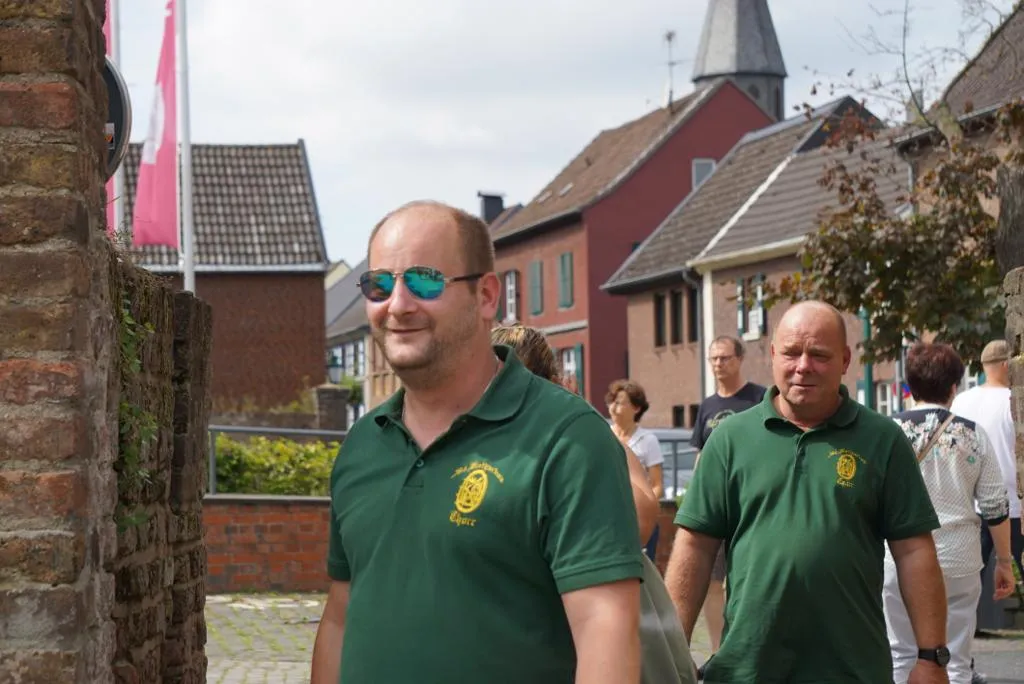 Zwei lachende Schützenbrüder vor einer Häuserzeile in Zons, im Hintergrund der Kirchturm