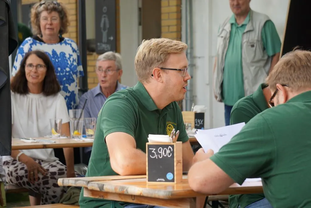 Vereinsmitglieder bei einer Pause in einem Café im Freien, eine Erdbeer-Bowle-Tafel mit 3,90 € vor sich
