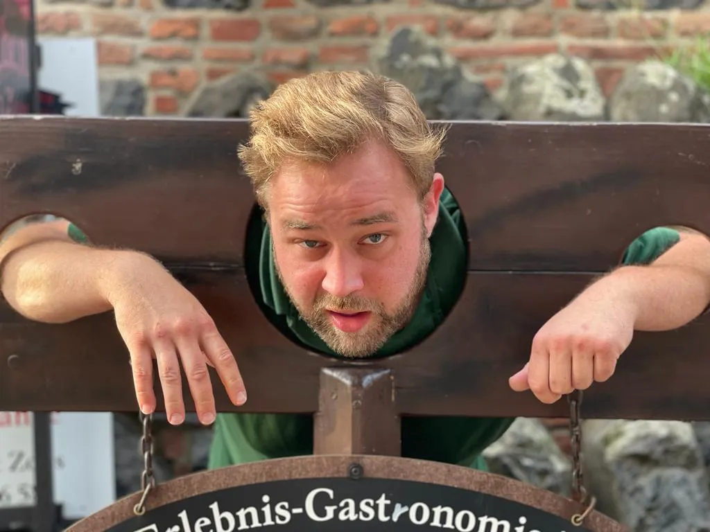 Schützenbruder steckt zum Spaß mit dem Kopf im hölzernen Pranger der Erlebnis-Gastronomie