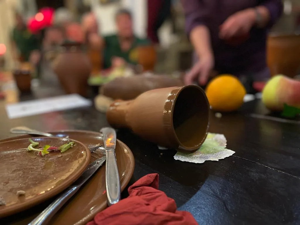 Detail der Mittelaltermahl-Tafel mit umgefallenem Tonbecher, Apfel und Orange