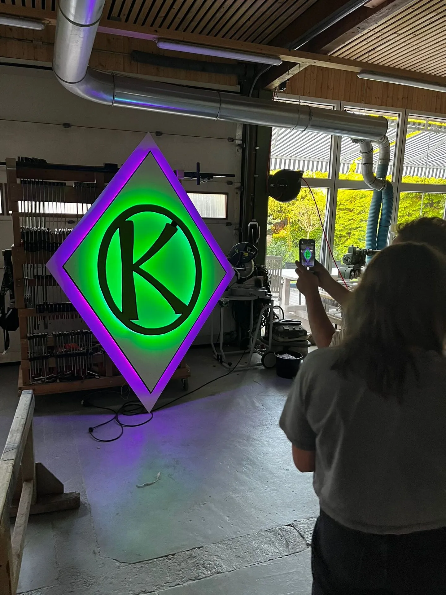 Helferin fotografiert das fertig verkabelte, beleuchtete K-Wappen-Schild in der Tischlerei