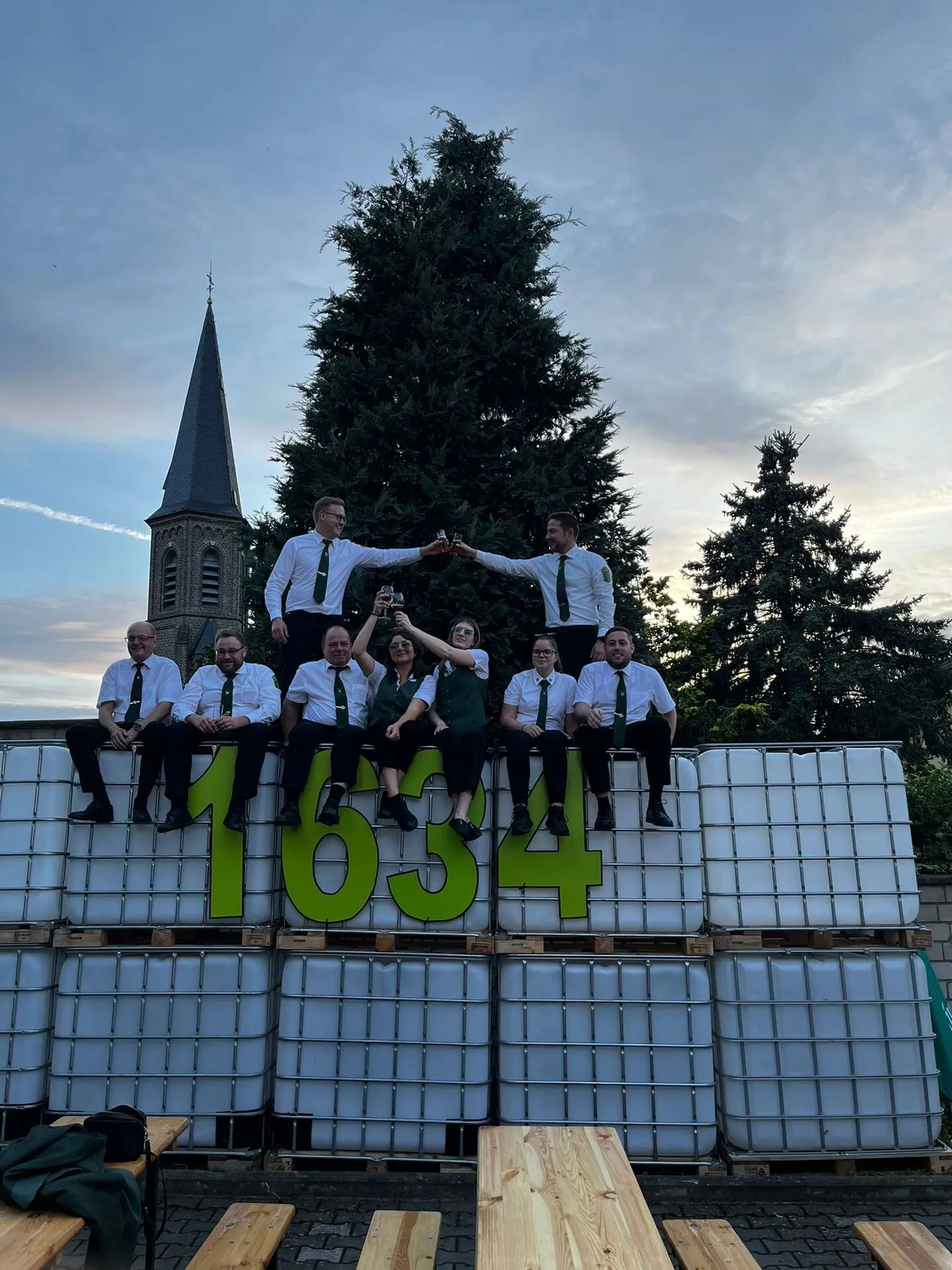 Junggesellen-Zug posiert auf der „1634"-Bühne aus weißen IBC-Tanks vor dem Kirchturm bei Sonnenuntergang