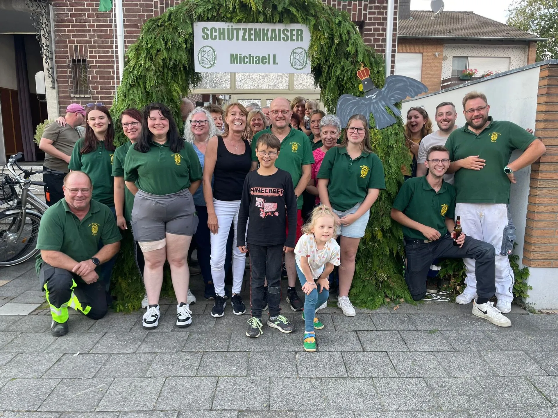 Gruppenbild des Vereins unter dem Tor-Bogen aus Tannengrün mit dem Schild „SCHÜTZENKAISER Michael I." am Haus des Schützenkaisers 2025